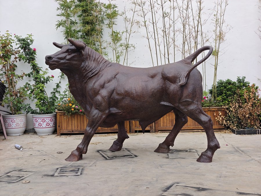 A bronze bull statue in a traditional Chinese garden setting