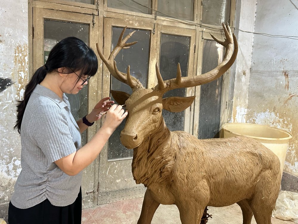 An artist making adjustments to a clay model of an elk based on client feedback.
